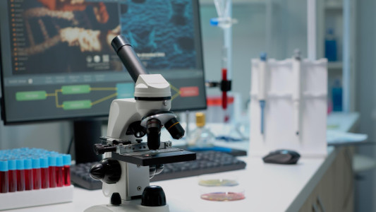 close-up-of-chemical-microscope-and-medical-research-equipment-in-scientific-laboratory-liquid-examination-tool-with-glass-lens-and-blood-samples-in-vacutainers-on-professional-desk